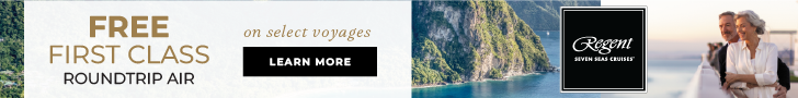Promotional ad for Regent Seven Seas Cruises. Background shows a tropical coastline with a mountain rising above turquoise water. The Regent logo appears at the top. Large text reads “Free First Class Roundtrip Air on select voyages.” A black button below says “Learn More.”
