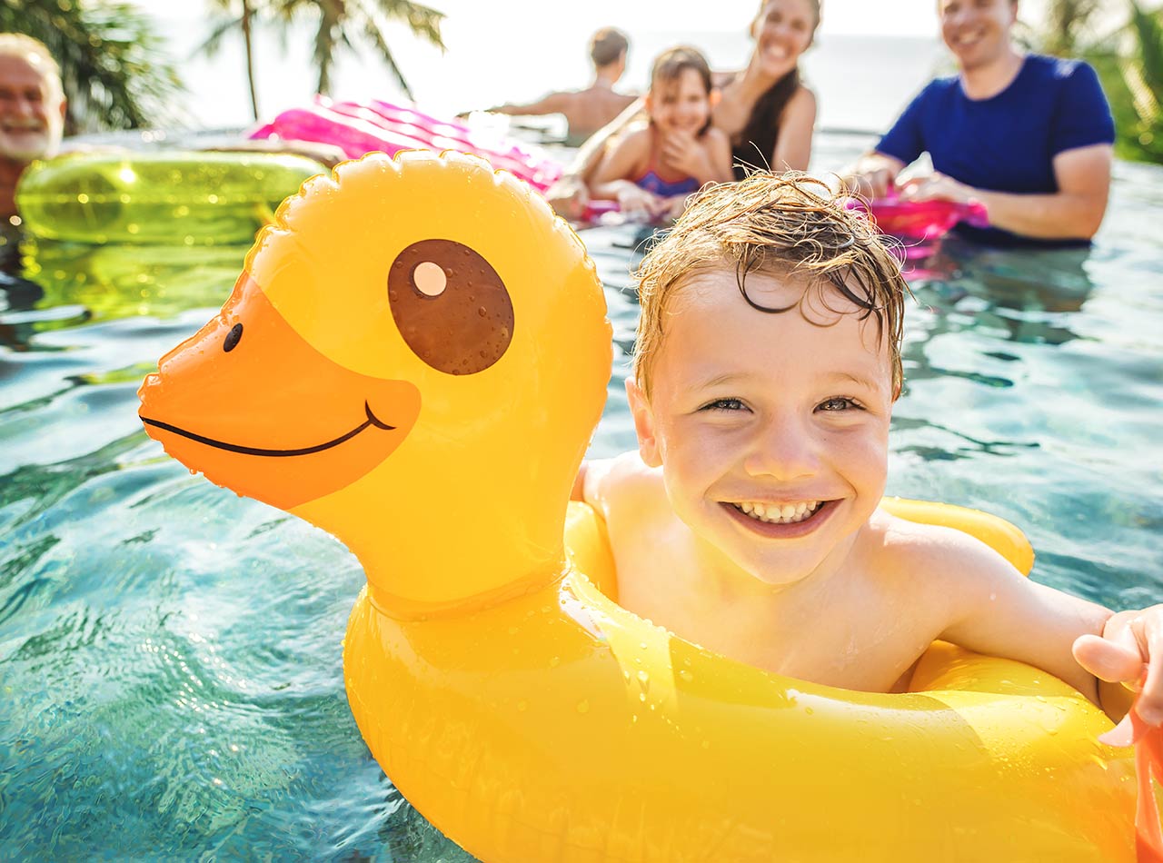 Boy swimming in resort pool with family and inflatable duck raft